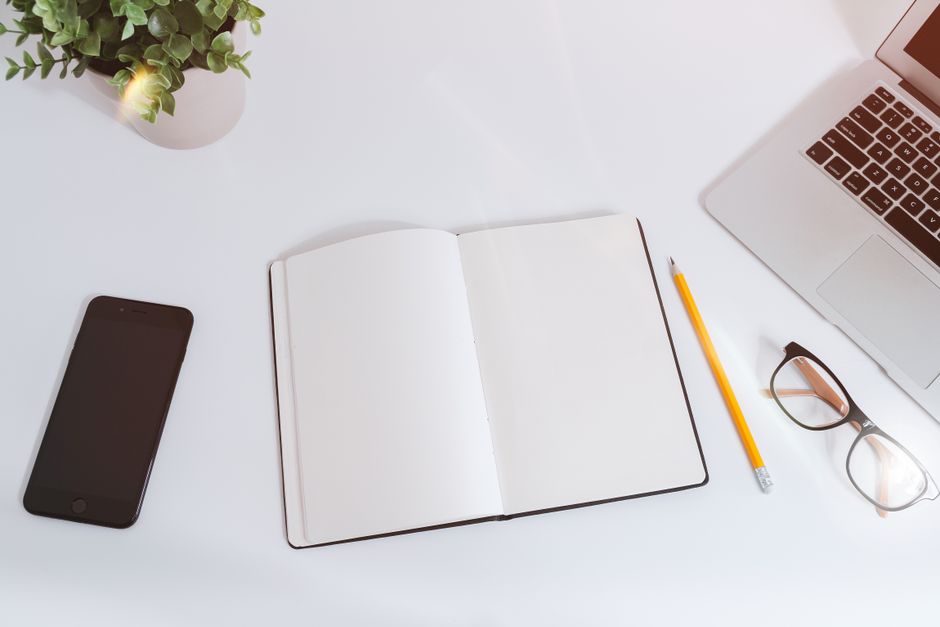 An organized workspace with a notebook, smartphone, and laptop on a bright, clean desk.